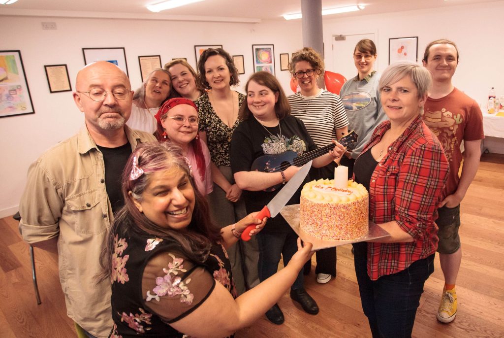 The VICS team and arts representatives of all ages, races and genders huddling round a cake to celebrate VICS 1st birthday